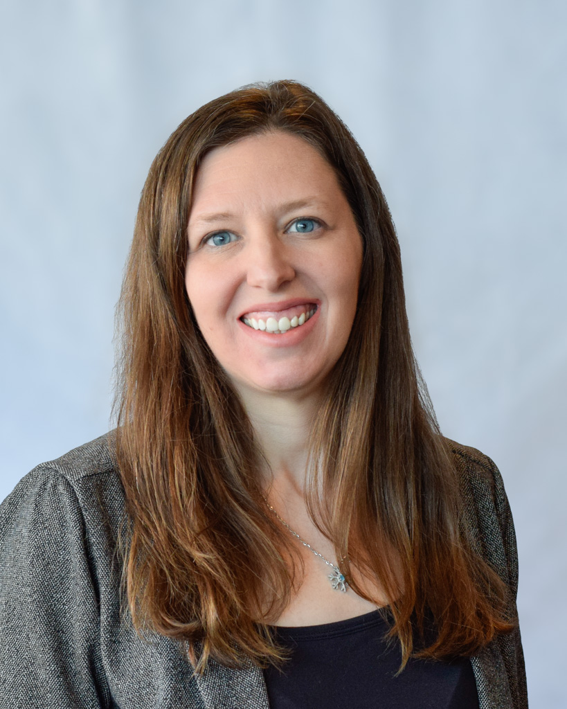 Woman with long brown hair and blue eyes smiling in a suit